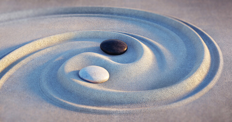 beratungsmethoden Das Foto zeigt ein mit Sand und zwei Steinen dargestelltes Yin und Yang Symbol. Die Steine sind weiß und schwarz. Dieses Symbol steht für die systemischen Werte in der Beratung.